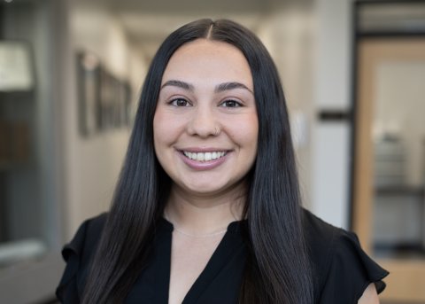Megan White, with long dark hair and a black top, smiles at the camera.