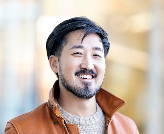 Jason Koo, in beige sweater and orange jacket, smiles at the camera.