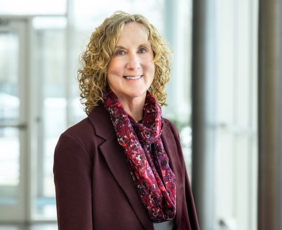 Dr Ann Damiano, in a purple blazer and scarf, stands by glass windows.